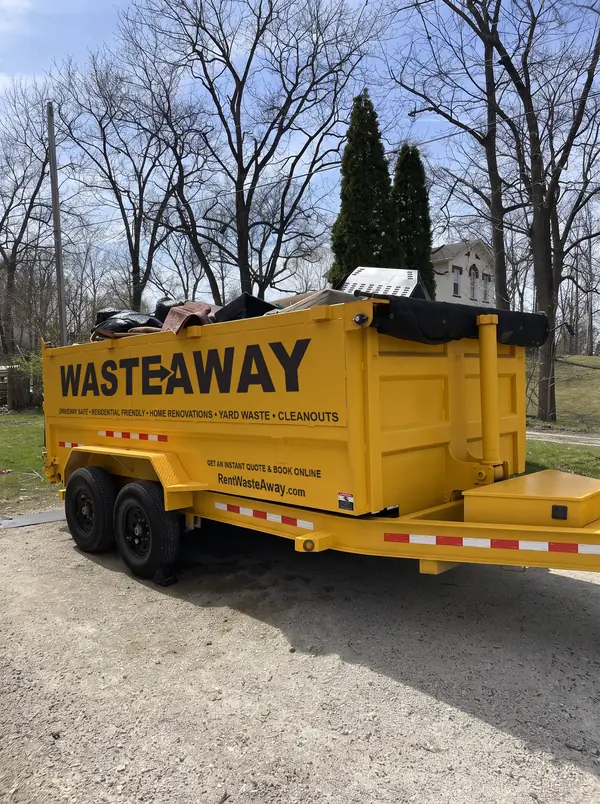 Dumpster on a gravel drive loaded with furniture and household junk